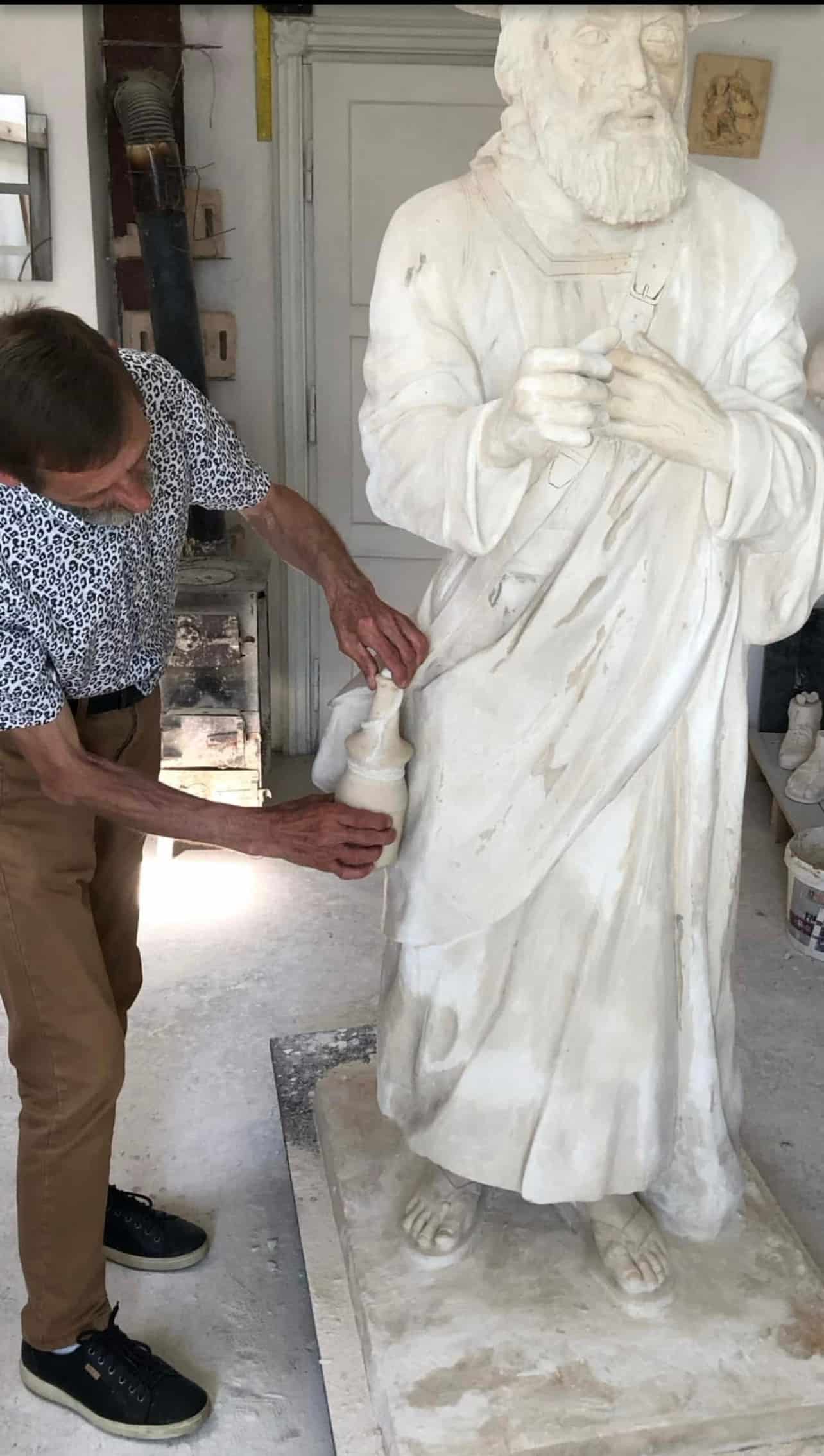 Rzeźbiarz pracujący w pracowni nad białym pomnikiem św. biskupa Józefa Sebastiana Pelczara, przedstawionego w szatach liturgicznych.